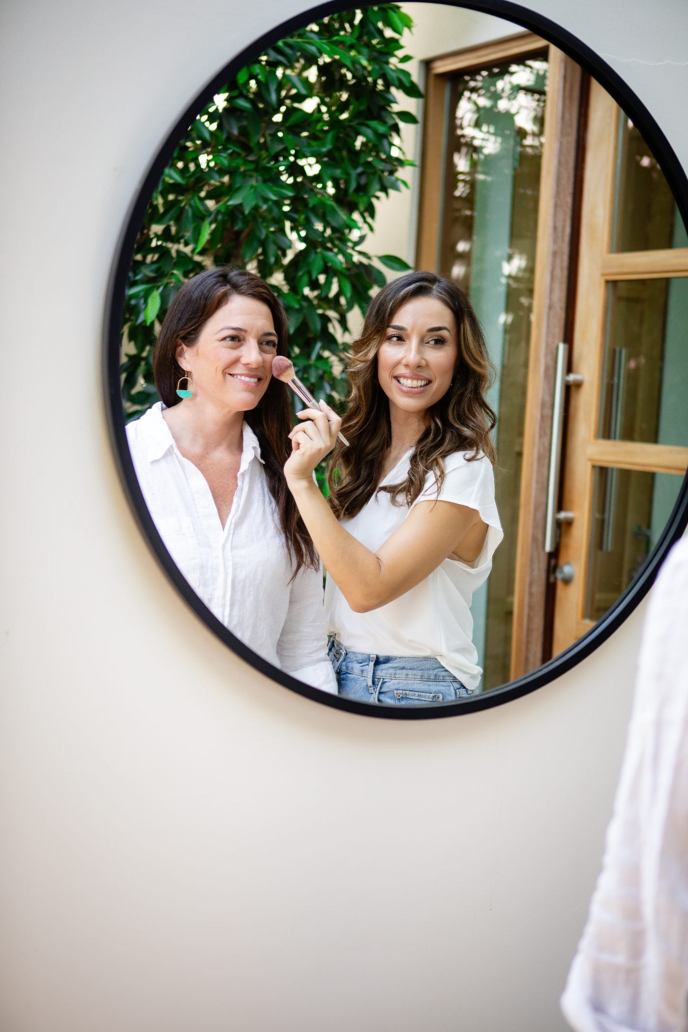 Yana applying makeup to a client in a round mirror